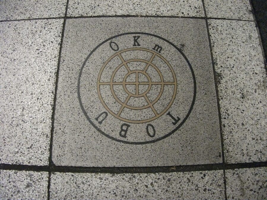 0 km post on the Tobu Isesaki Line at Kita-Senju Station platform with Tobu's wheel-and-east emblem